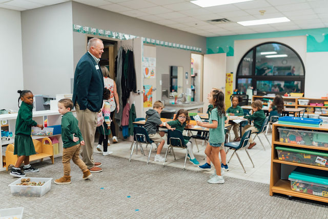 A grandparent with a visitor sticker visiting a preschool classroom.