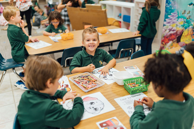 Kindergarten students coloring together at a classroom table.
