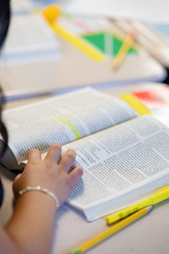 Hand resting on an open Bible with highlighted text and a highlighter