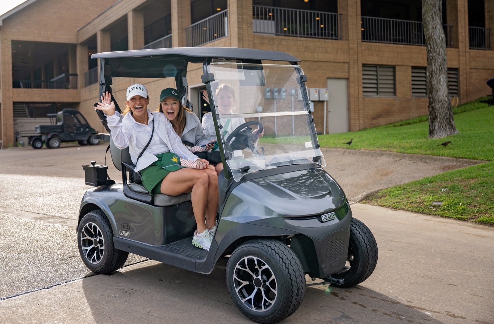 Players smiling and waving from a golf cart